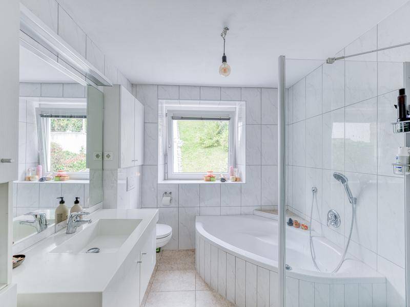 Helles Badezimmer mit weißen Fliesen, Badewanne, Dusche und Fenster.