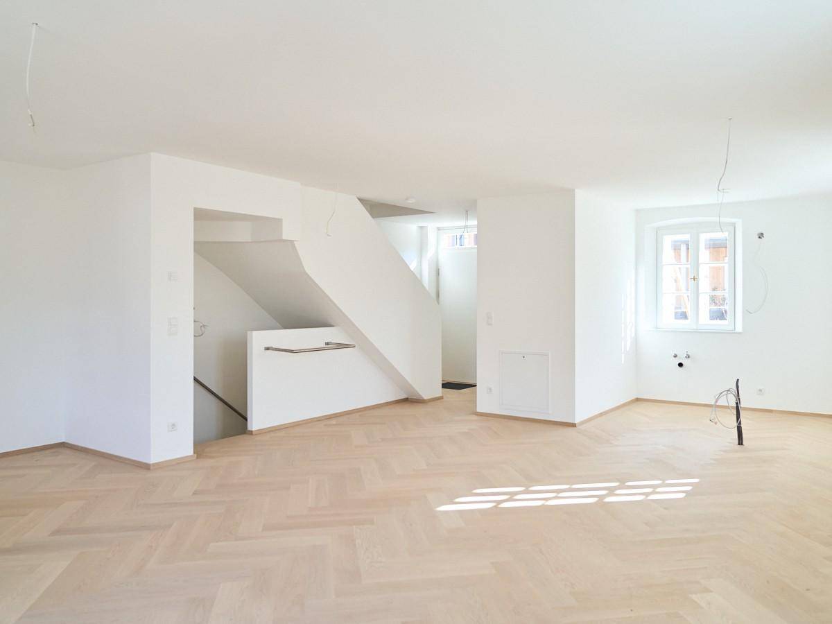 Heller Wohnbereich mit elegantem Fischgrätparkett und offener Treppe.