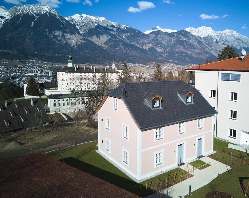 Gesamtansicht des Neubaus mit gepflegtem Garten und majestätischem Bergpanorama.