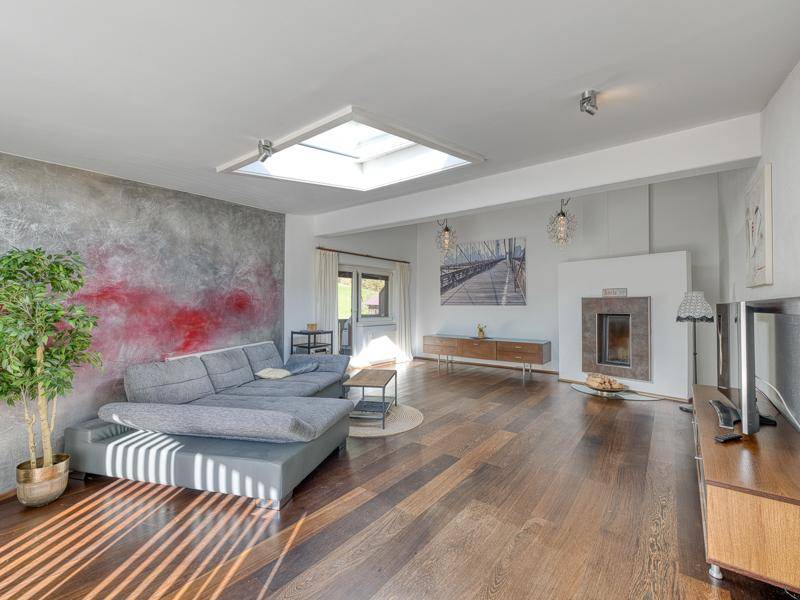 Gemütliches Wohnzimmer mit modernem Kamin, großem Sofa, Holzboden und Oberlicht für viel Tageslicht.