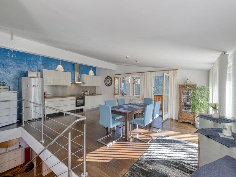Heller offener Wohn- und Essbereich mit moderner Küche, Holzboden und Zugang zum Balkon.