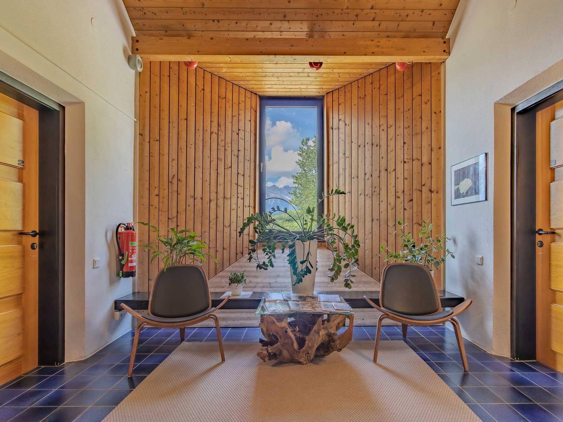 Einladender Flur mit Holzverkleidung, blauen Fliesen und Blick ins Grüne durch das Fenster.
