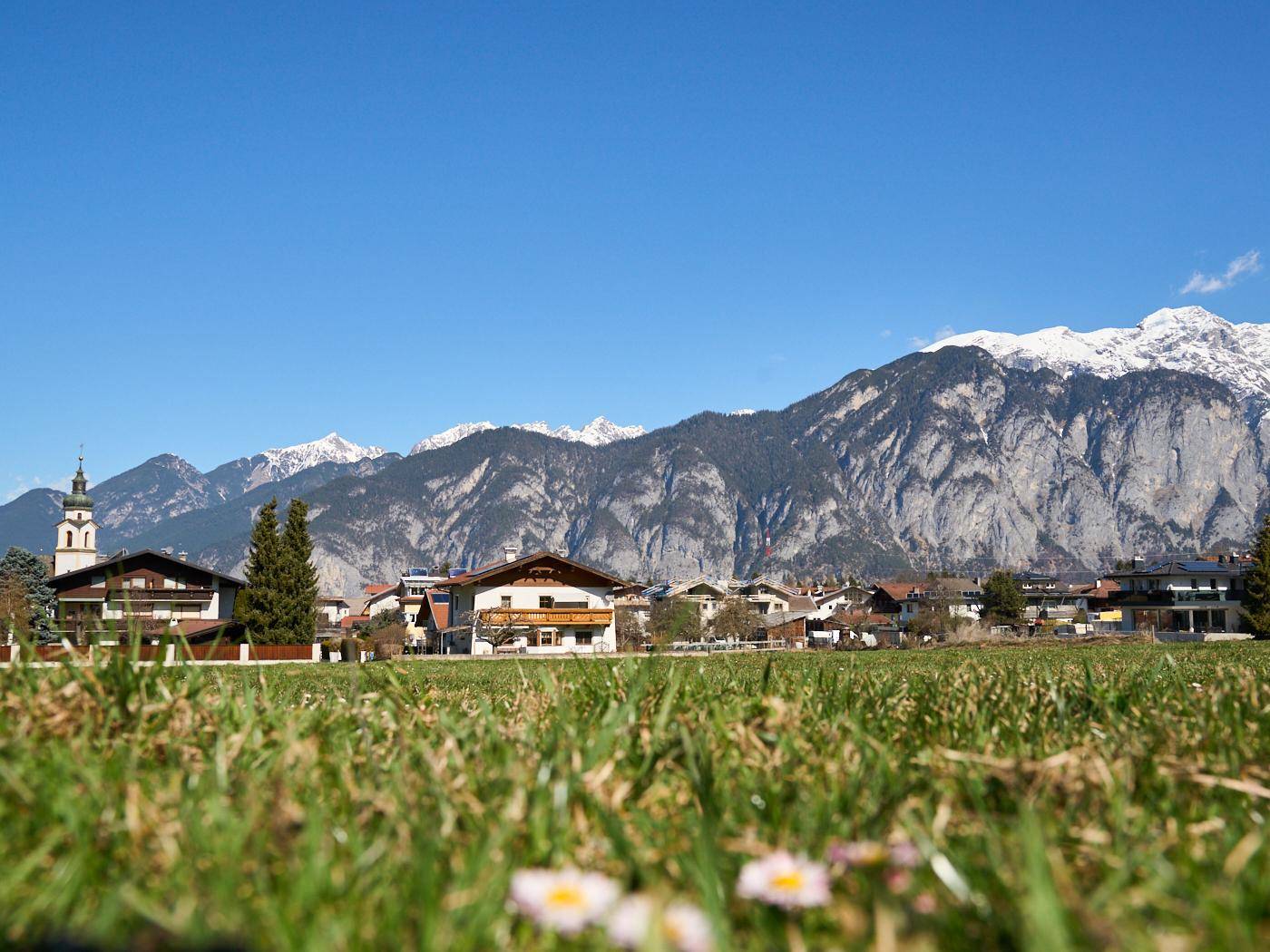 Idyllische Wiesenlandschaft mit Blick auf ein malerisches Dorf und die majestätischen Alpen im Hintergrund.