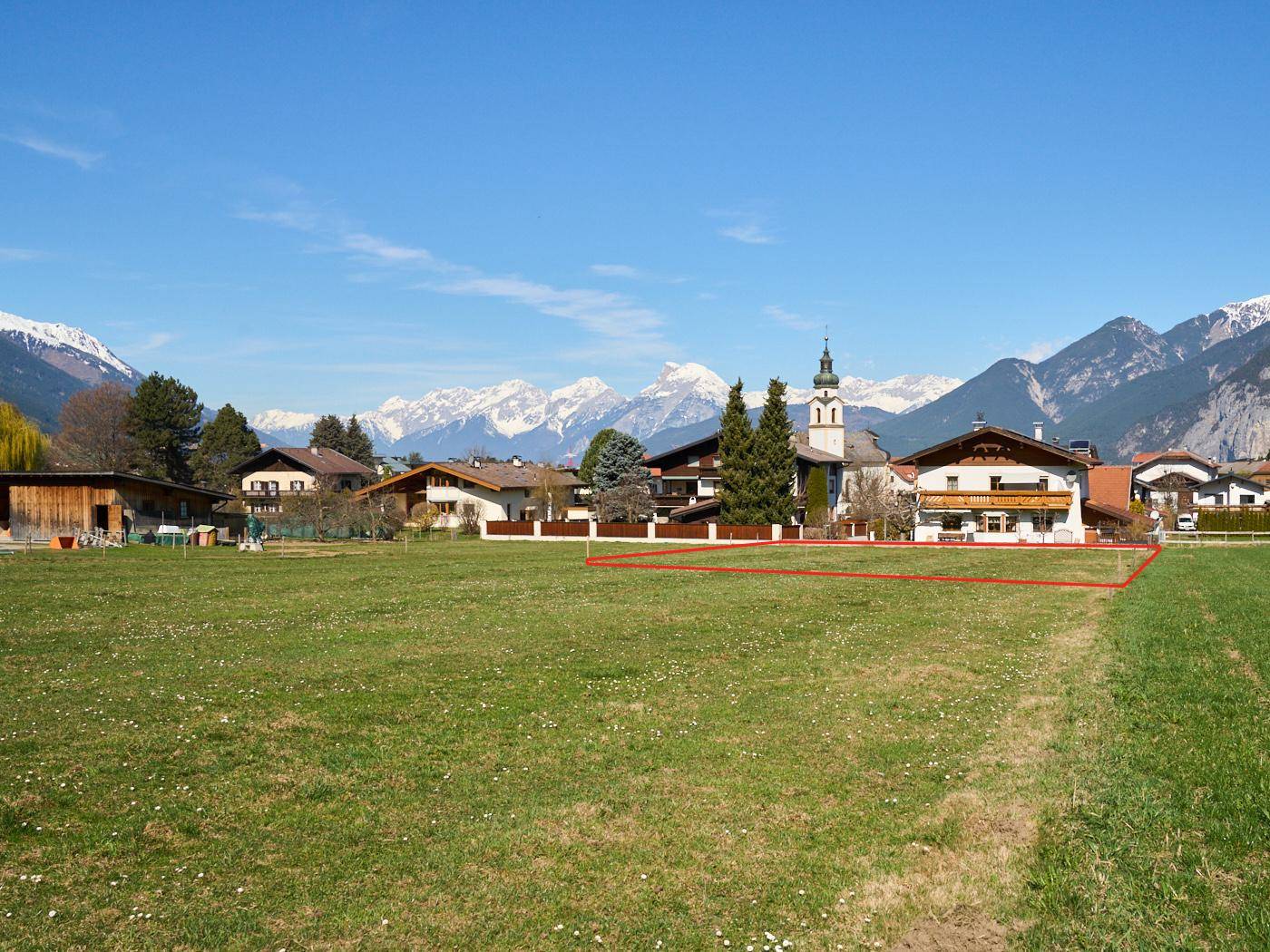 Grünes Baugrundstück mit Blick auf ein charmantes Dorf und die beeindruckende Berglandschaft.