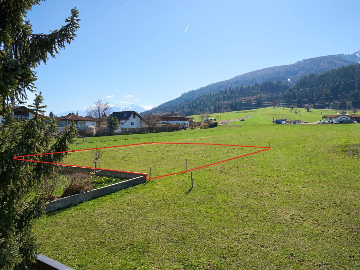 Weitläufiges grünes Grundstück mit roter Markierung, umgeben von sanften Hügeln und Wohnbebauung.