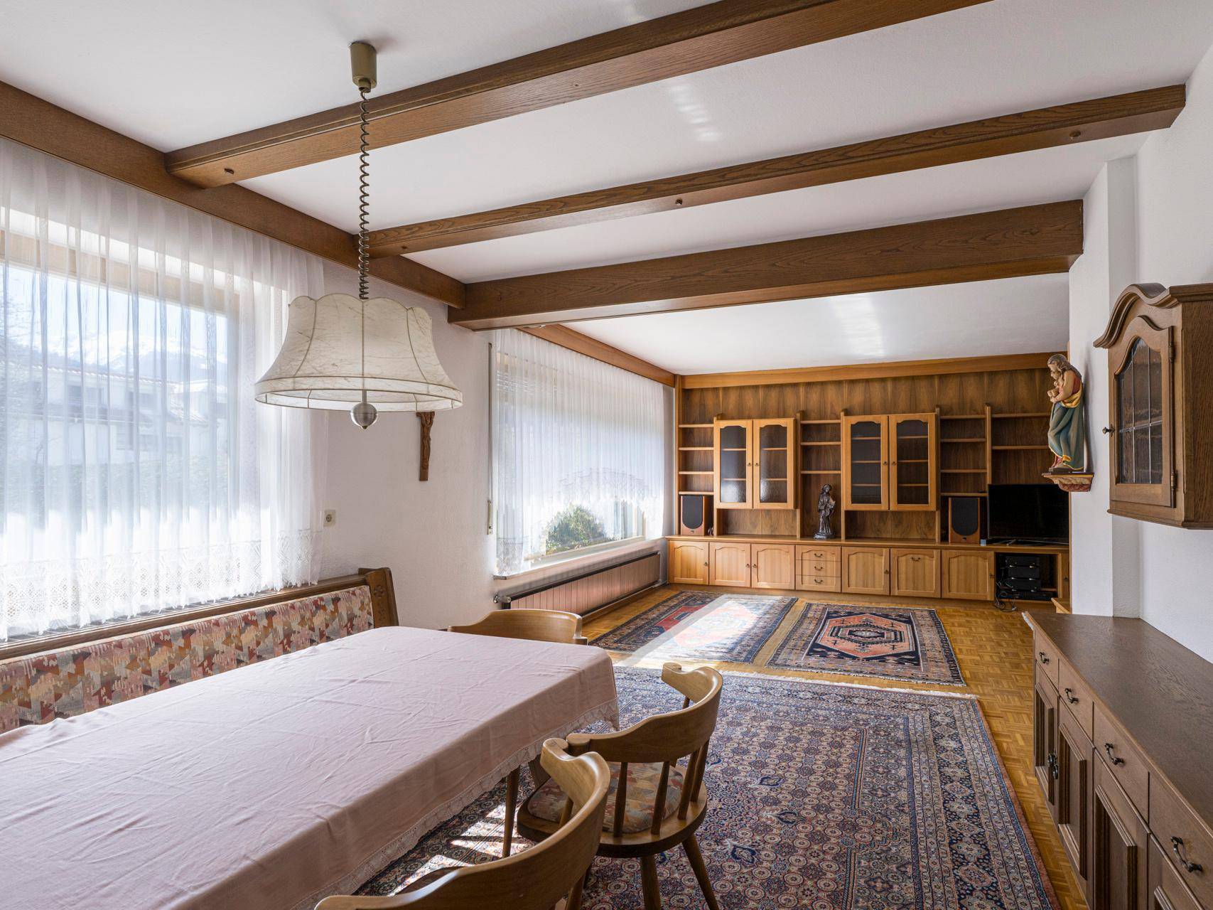 Gemütlicher Wohn-Essbereich mit Holzbalkendecke, traditionellen Möbeln und großen Fenstern.