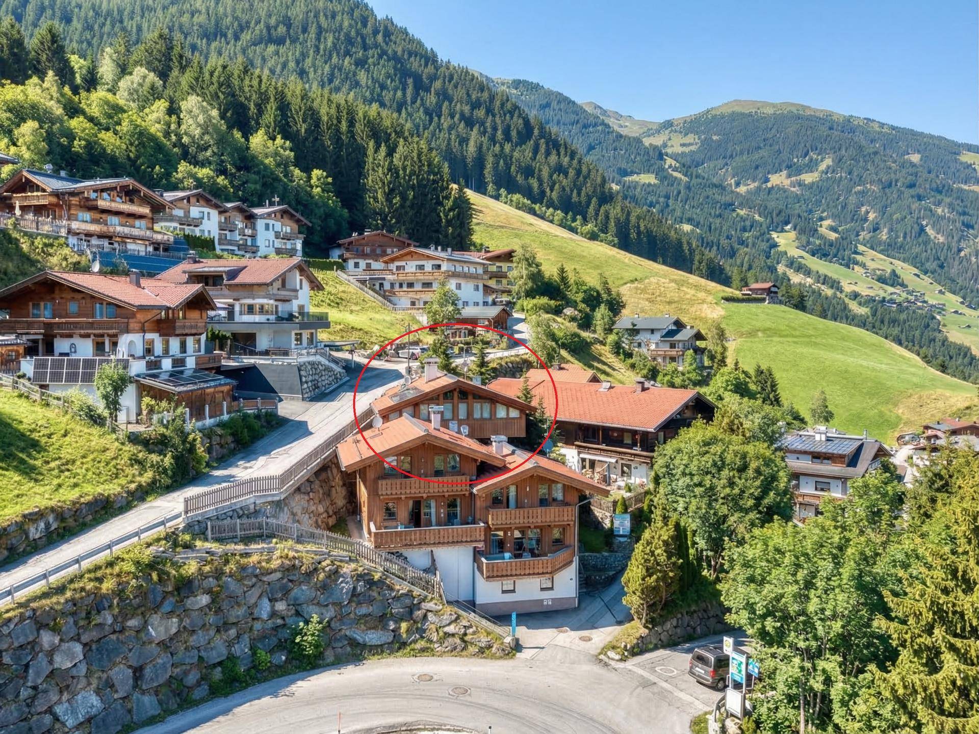 Luftaufnahme eines charmanten Bergdorfes in alpiner Landschaft, mit einem markierten Gebäude im Zentrum.