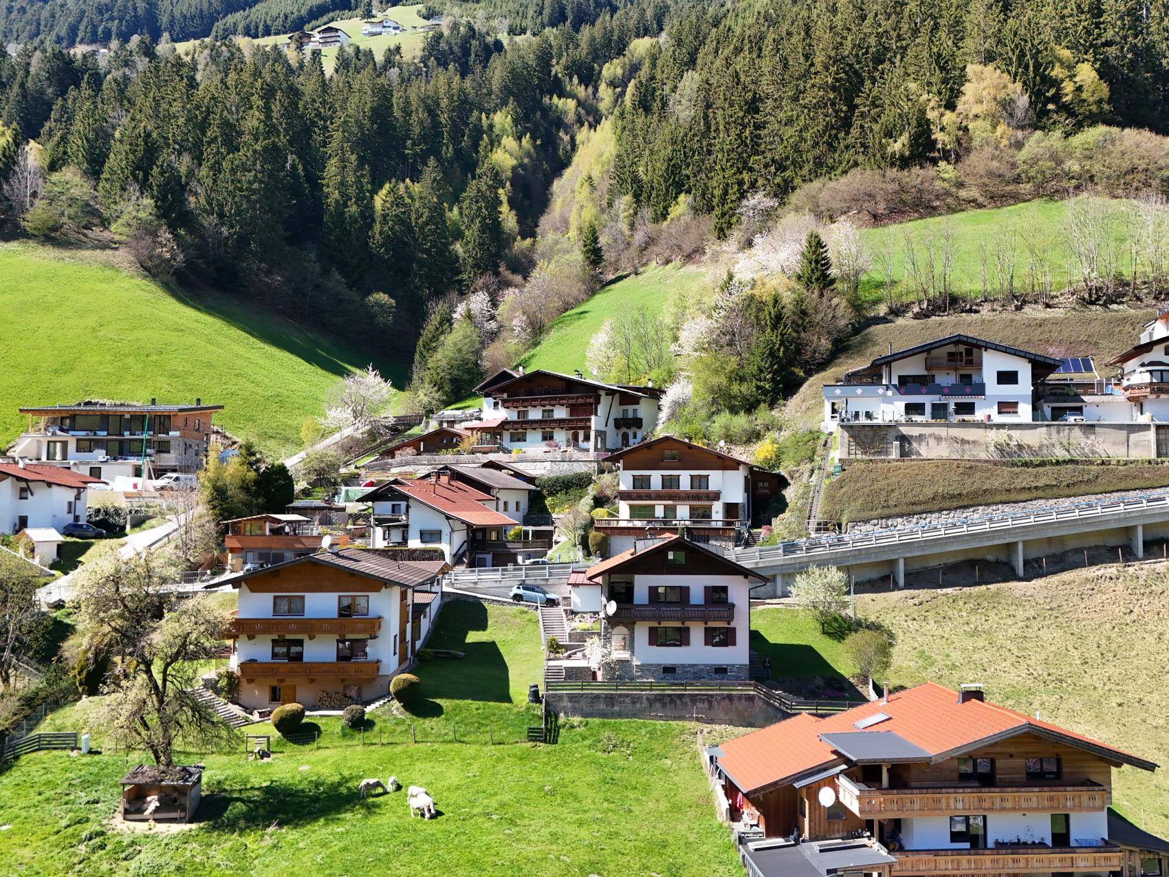 Panoramablick auf mehrere Häuser, eingebettet in eine grüne Berglandschaft unter blauem Himmel.