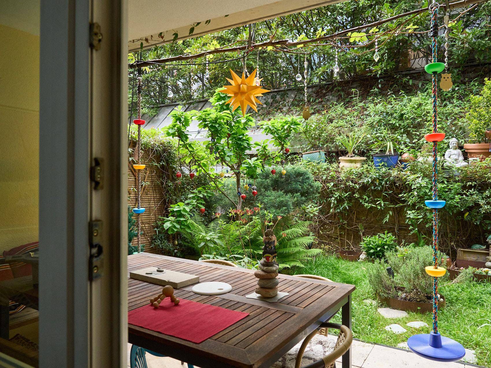 Gemütliche Terrasse mit Holztisch und Stühlen, umgeben von einem dichten, grünen Garten.