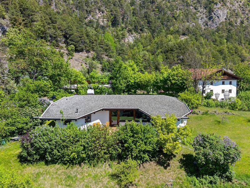 Haus in Hanglage umgeben von grüner Natur mit Blick auf die umliegenden Berge.