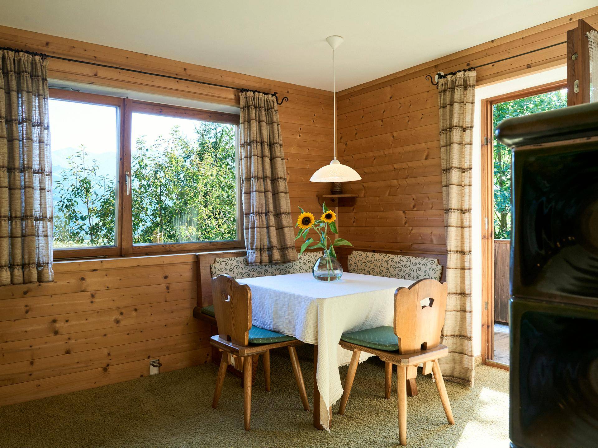 Gemütlicher Essbereich im alpinen Stil mit Holzwänden, Kachelofen und Blick ins Grüne.