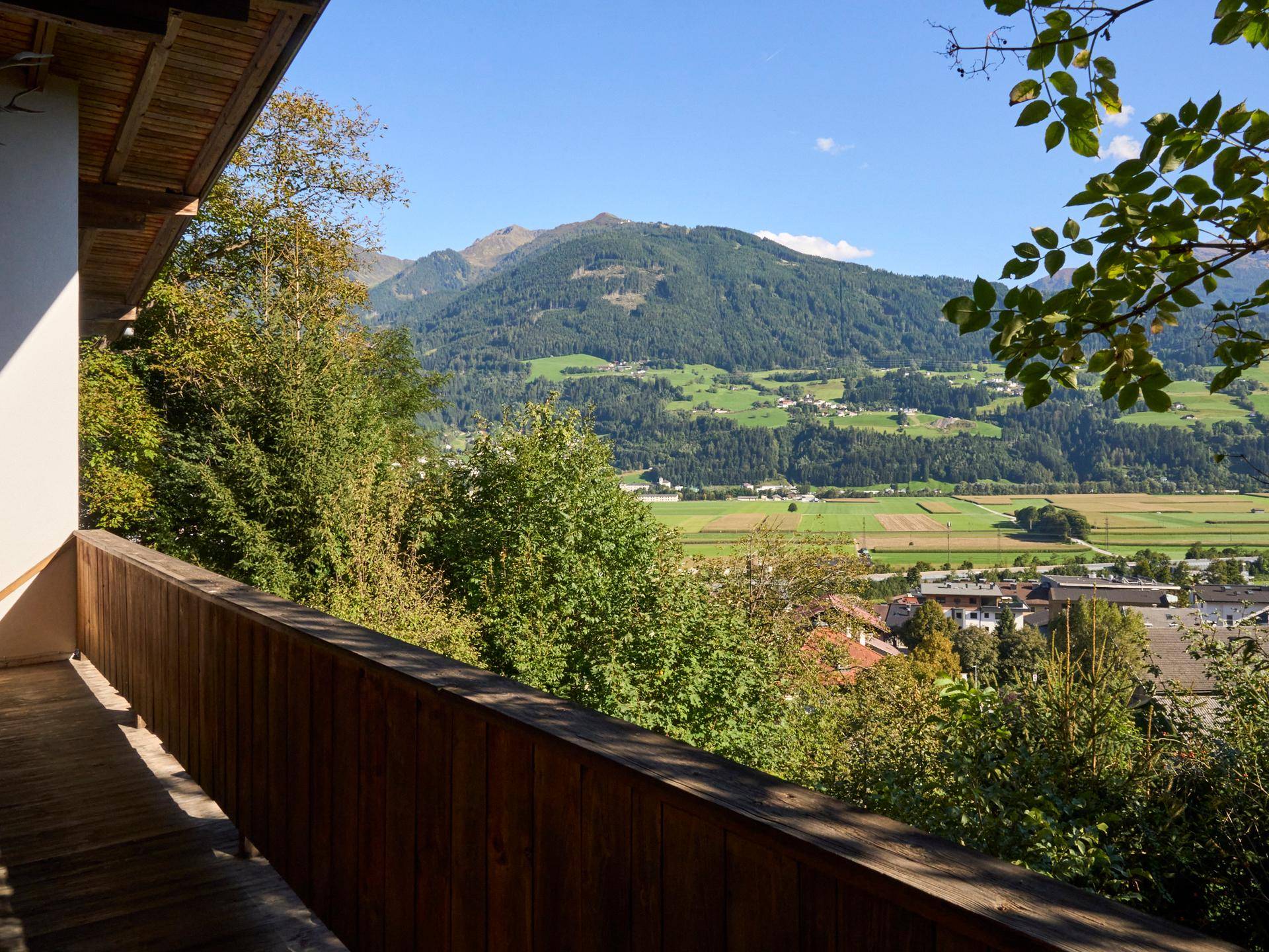 Panoramablick vom Holzbalkon über das Tal mit grünen Wiesen und majestätischen Bergen.