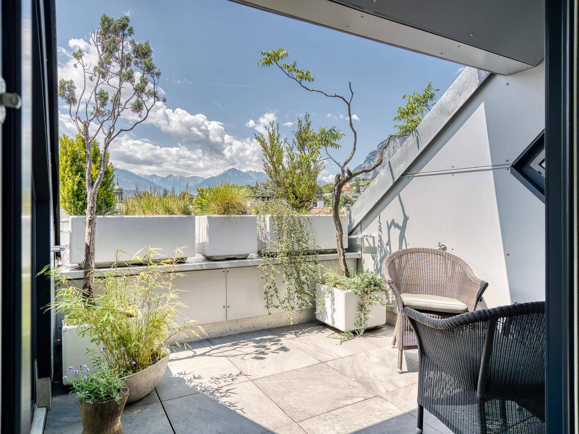 Sonnige Dachterrasse mit bequemen Sitzgelegenheiten, Pflanzen und einem weiten Blick auf die Berge.