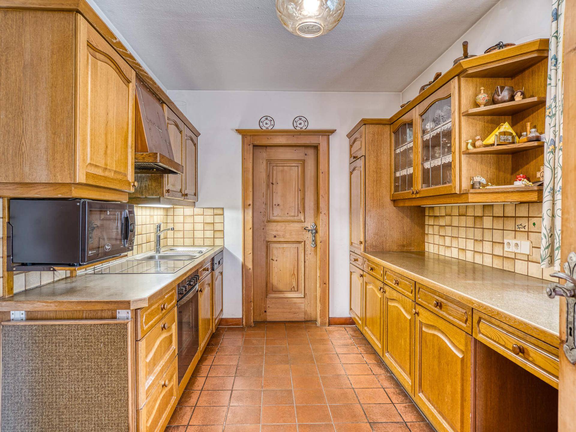 Traditionelle Holzküche mit Einbauschränken, Fliesenrückwand und Terrakottafliesen.