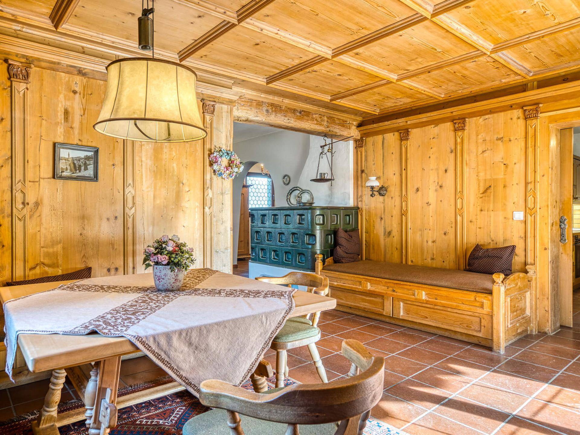 Rustikaler Essbereich mit Holztisch, Eckbank und traditionellem Kachelofen.