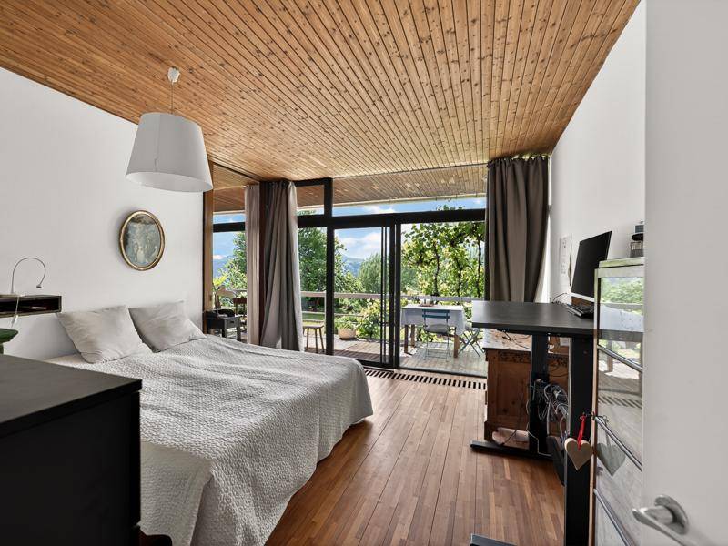 Helles Schlafzimmer mit Holzboden und Holzdecke, großen Fenstern und Zugang zum Außenbereich.