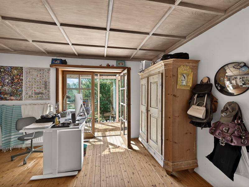 Arbeitszimmer mit Holzboden, Holzdecke und einem traditionellen Kleiderschrank, mit Blick ins Grüne.