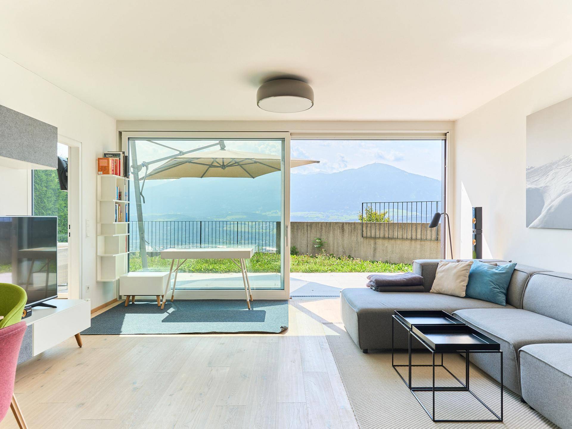Helles Wohnzimmer mit modernem Sofa, Holzboden und Zugang zur Terrasse mit Bergblick.