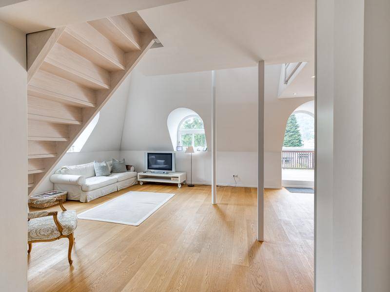 Gemütlicher Wohnbereich mit Holztreppe, Sofa und Blick ins Grüne durch das Rundbogenfenster.