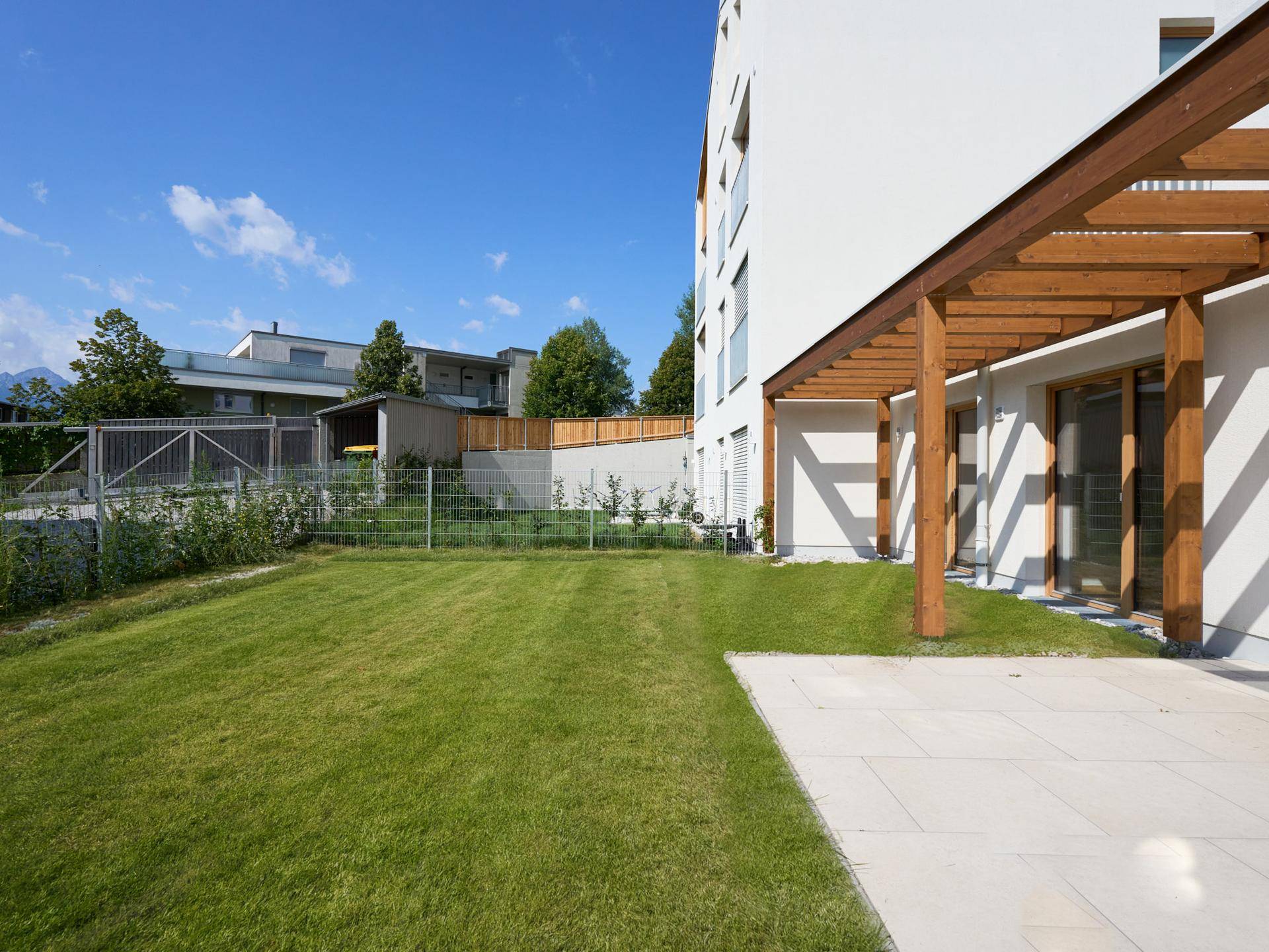 Weitläufiger Gartenbereich mit Rasenfläche und einer gepflasterten Terrasse neben dem Gebäude.