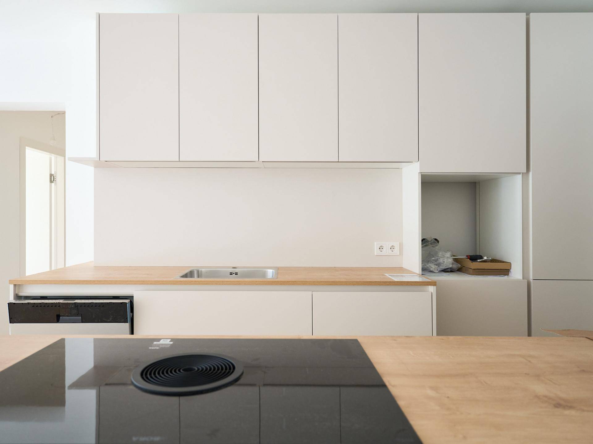 Moderne Einbauküche mit hellen Schränken, Holz-Arbeitsplatte und Induktionskochfeld.