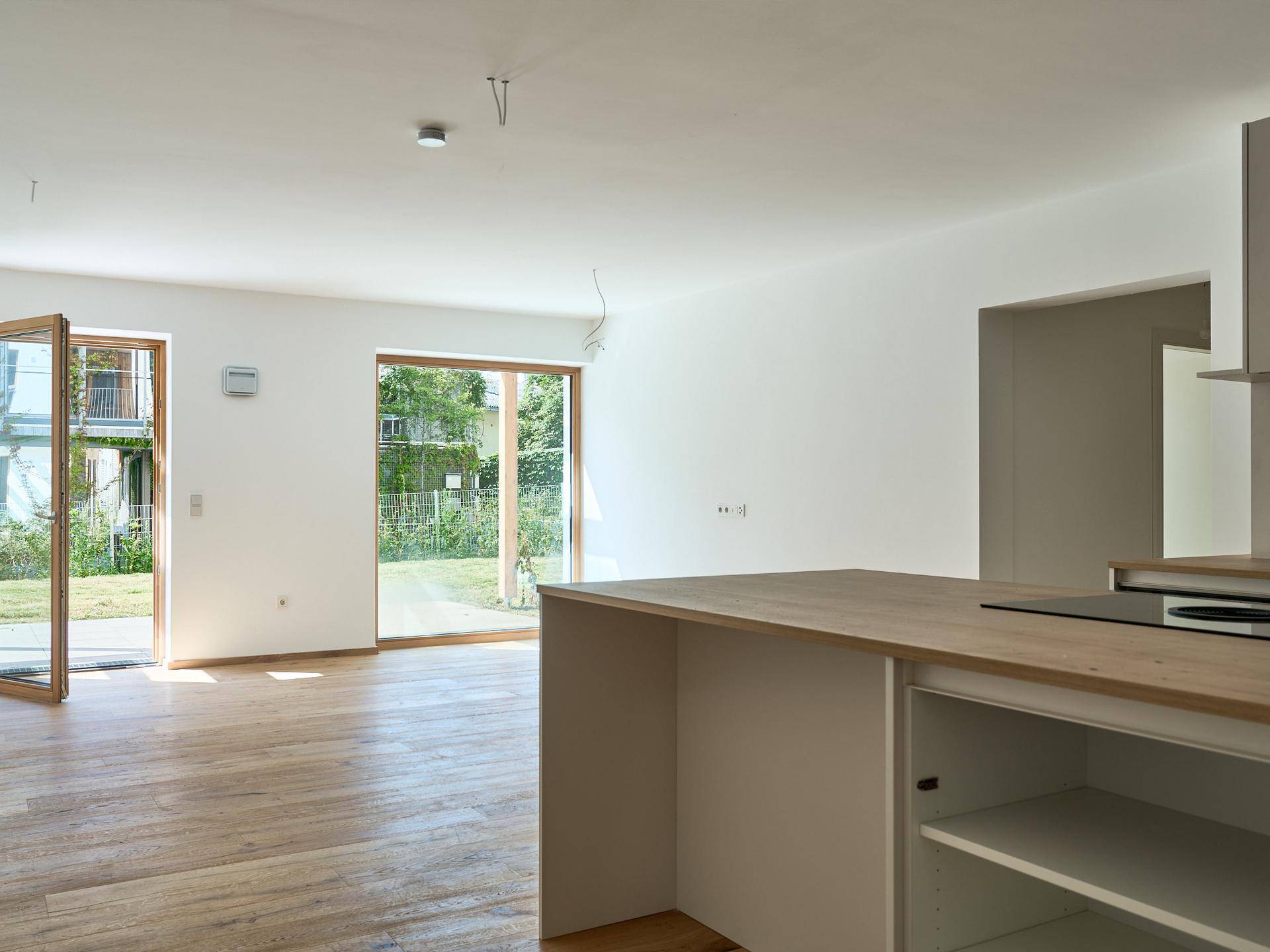 Heller offener Wohnbereich mit Holzboden, großen Fenstern und Zugang zum Garten.