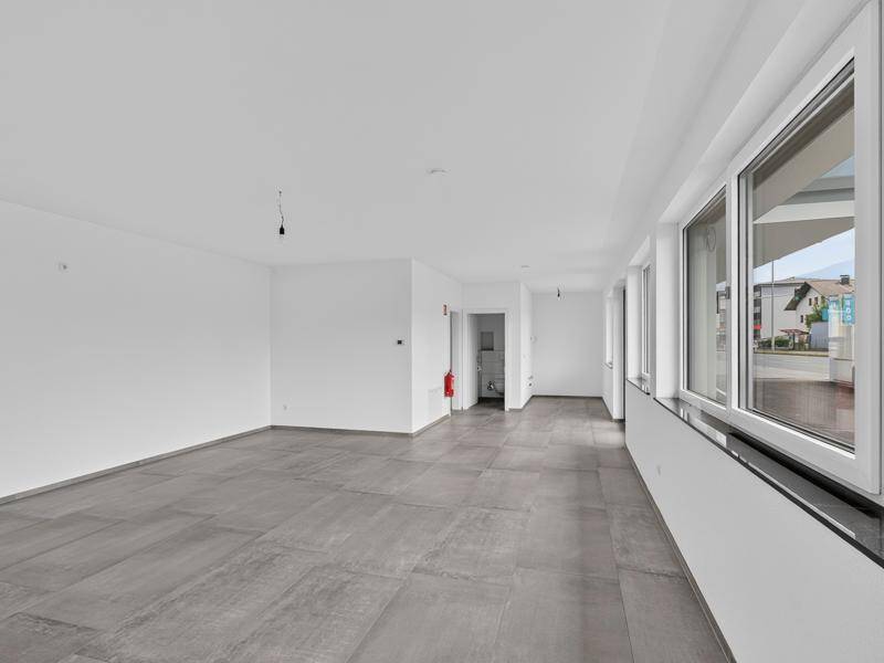 Heller, leerer Raum mit großen Fenstern entlang einer Wand und modernem Fliesenboden.