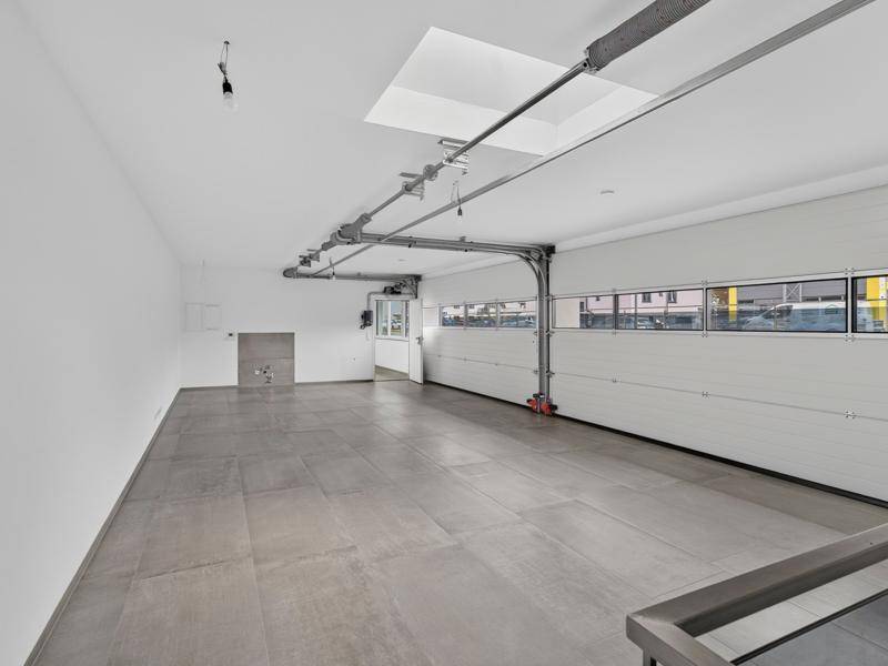 Geräumiger Garagenraum mit großem Rolltor, Fliesenboden und Oberlicht für natürliches Tageslicht.