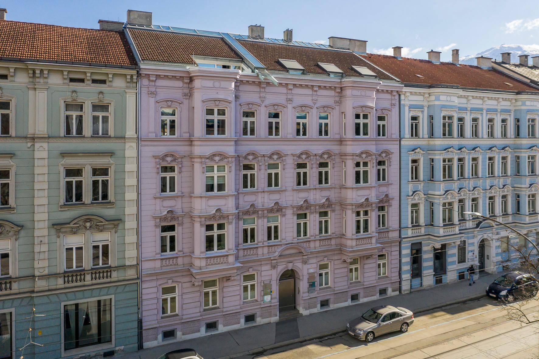 Historisches Gebäude mit aufwendiger Fassade und modernen Dachaufbauten in städtischer Umgebung.