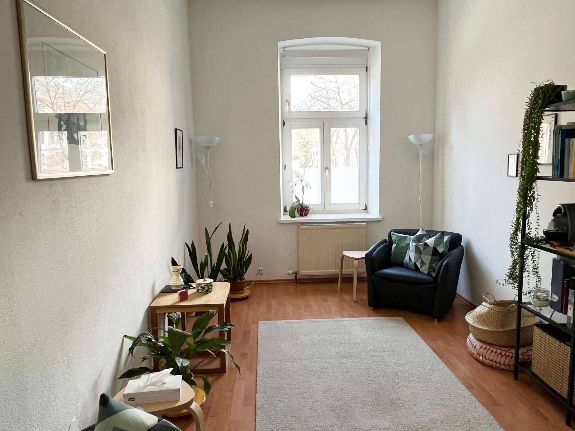 Lichtdurchfluteter Raum mit Holzboden, gemütlichem Sessel, Pflanzen und einem großen Fenster.