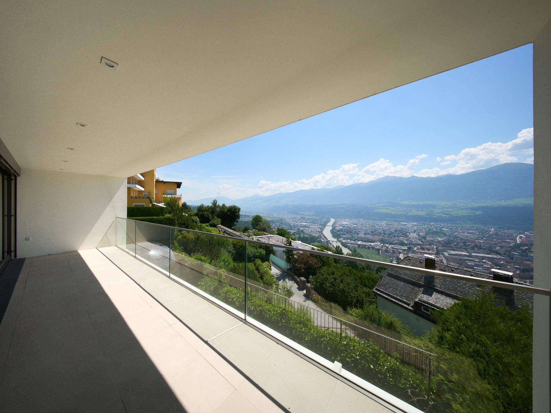 Geräumiger Balkon mit Glasgeländer und weitem Blick auf die Stadt und die umliegende Berglandschaft.