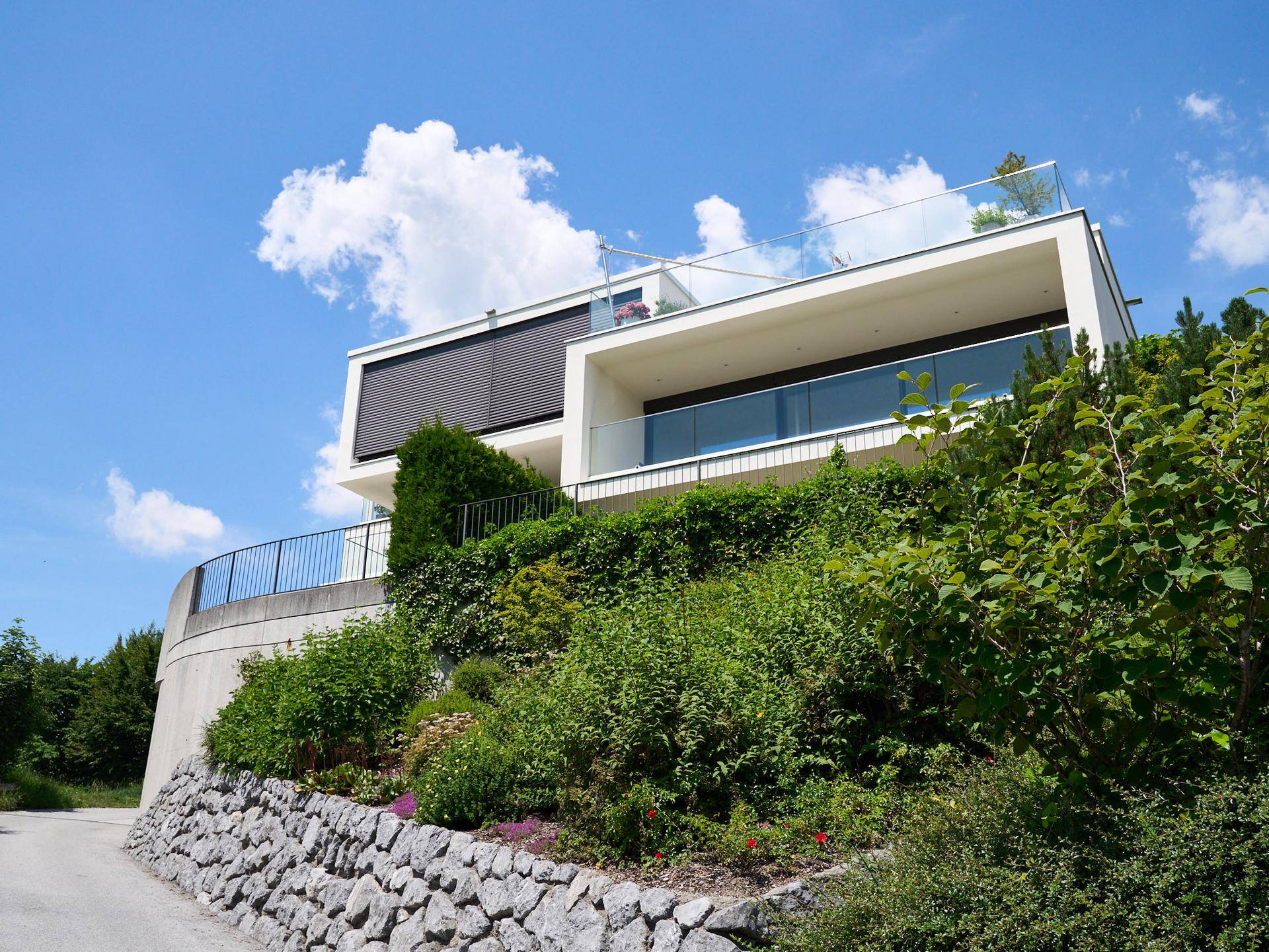 Moderne Architektur auf einem Hügel mit viel Grün und klarem Himmel.