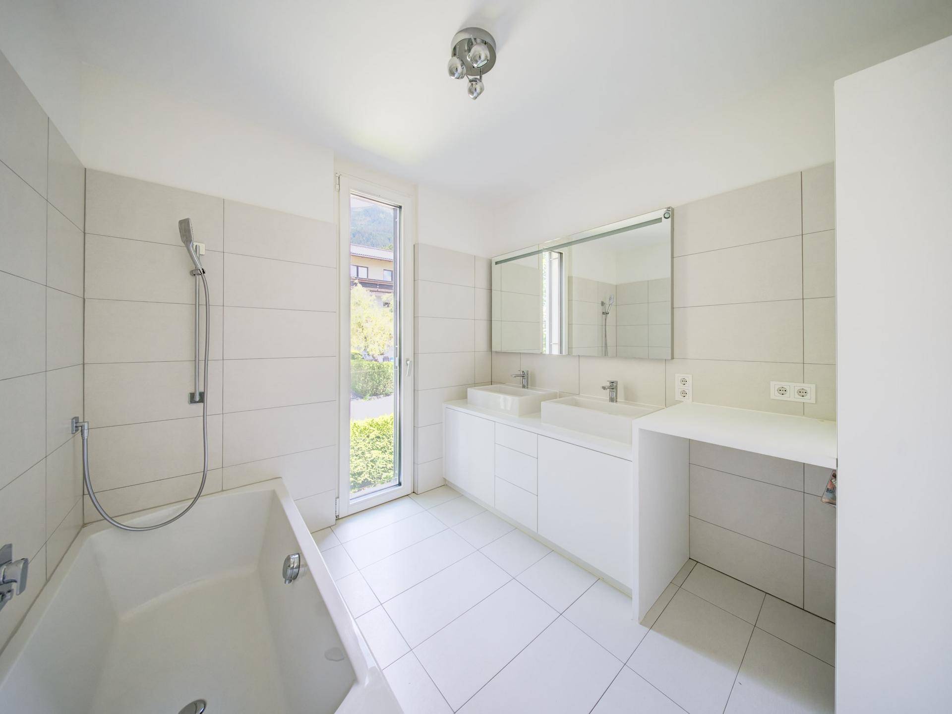 Modernes Badezimmer mit Doppelwaschbecken, Badewanne und Fenster für Tageslicht.