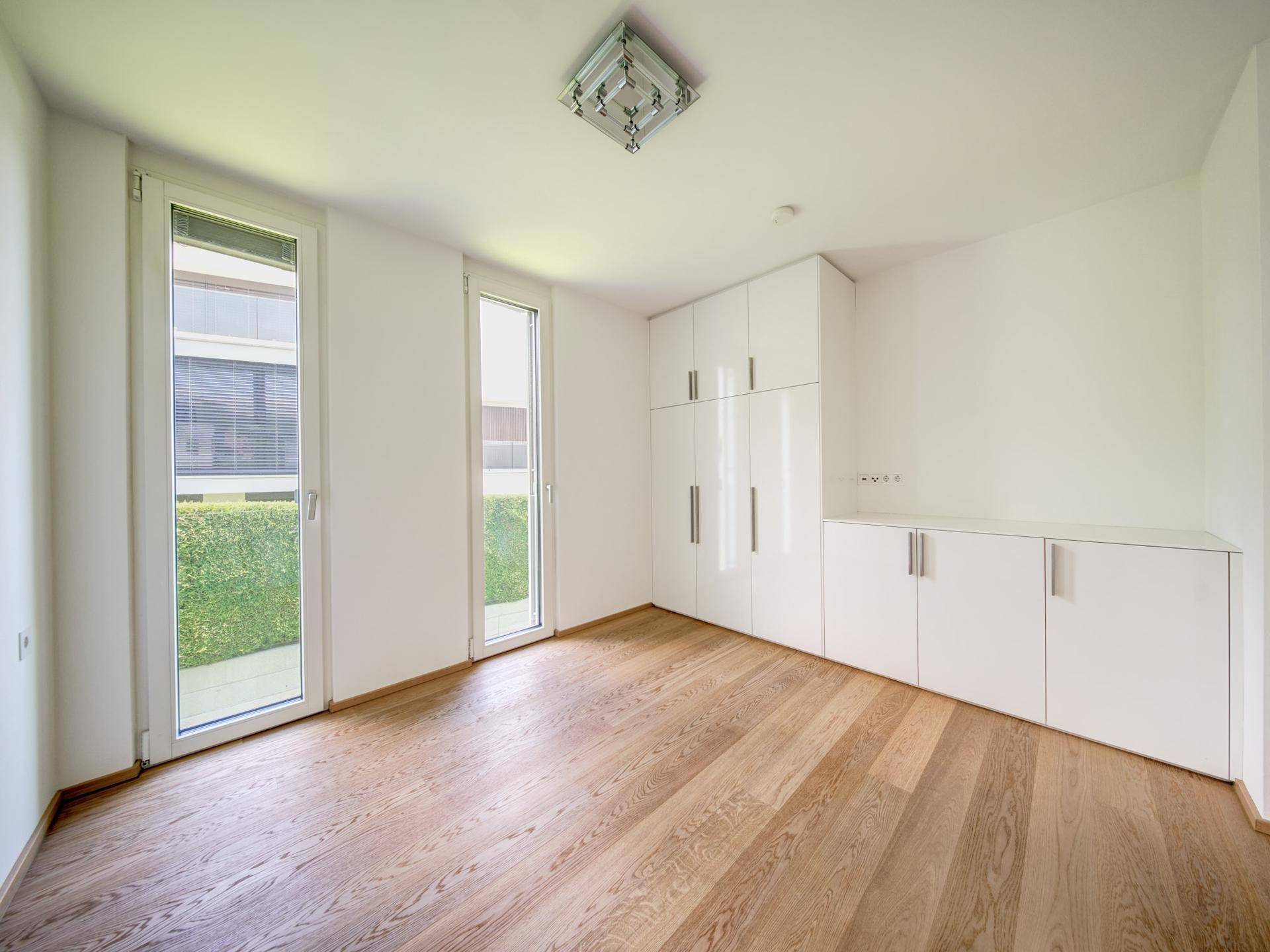 Helles Zimmer mit Holzboden, weißen Einbauschränken und Zugang zum Gartenbereich.