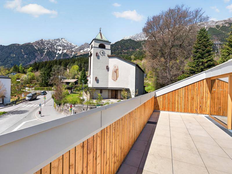 Terrasse mit Holzwänden und Blick auf eine Kirche, die Straße und die majestätische Bergwelt.