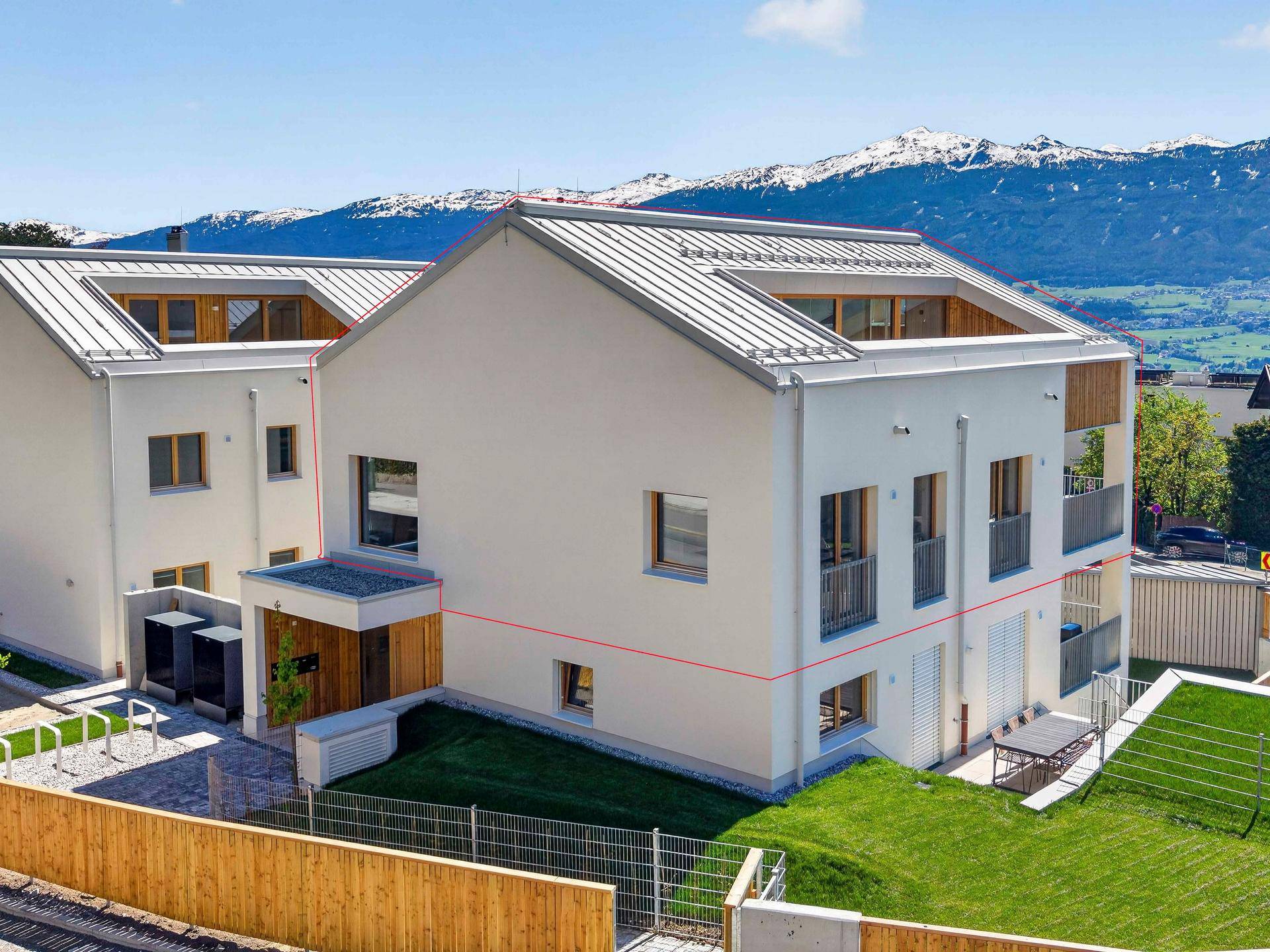 Zwei moderne Neubauten mit gepflegten Rasenflächen und beeindruckendem Bergpanorama im Hintergrund.
