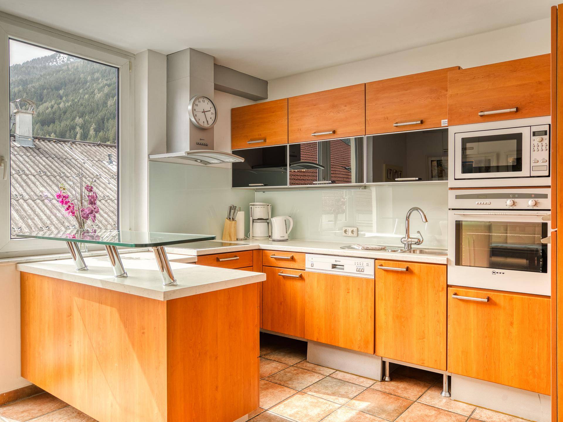 Moderne Holzküche mit Einbaugeräten, Fliesenboden und Fenster mit Bergblick.