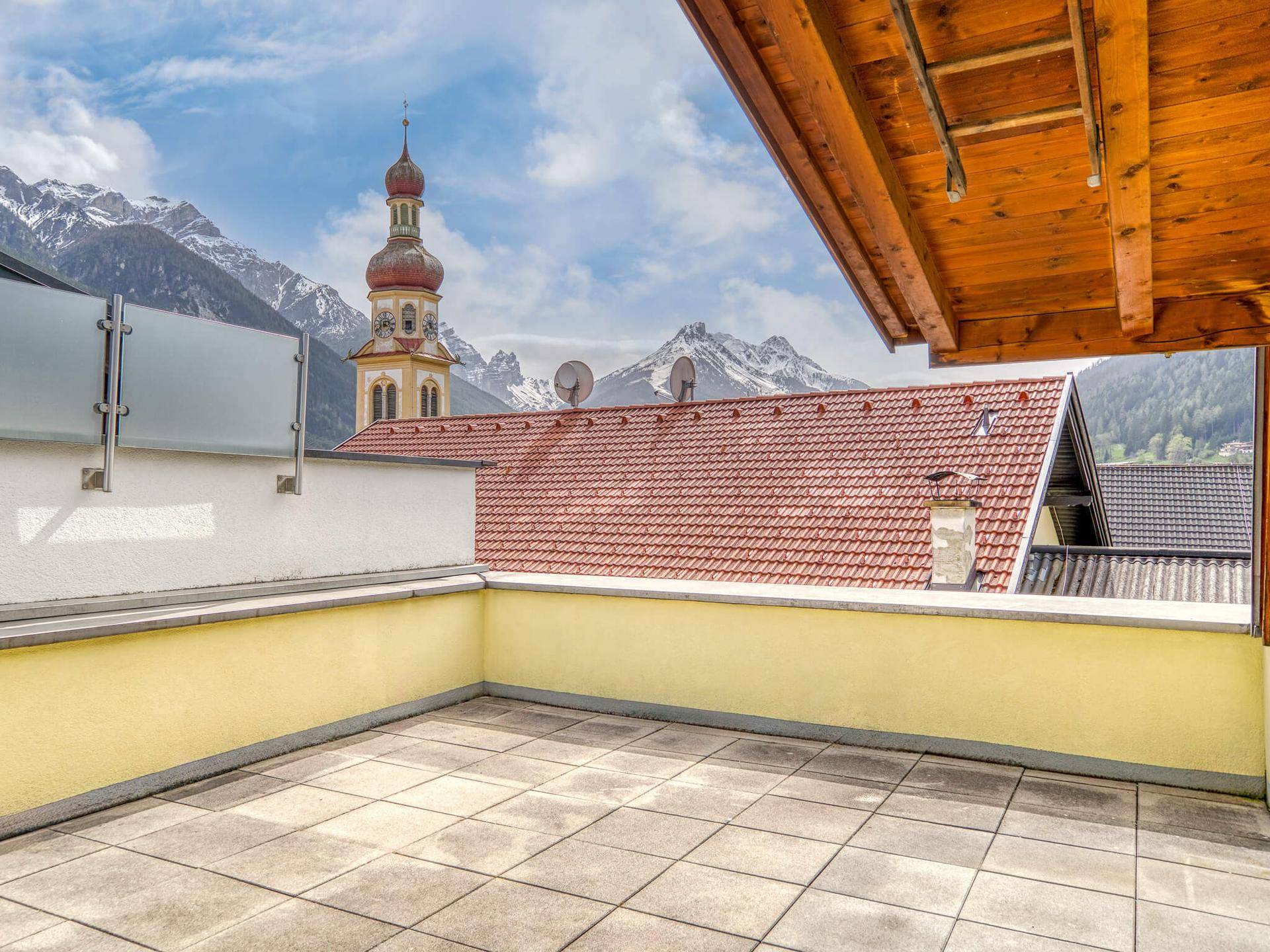 Sonnenterrasse mit Panoramablick auf die Berge und eine historische Kirche.