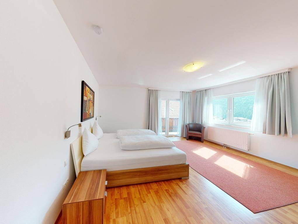 Helles Schlafzimmer mit Doppelbett, Holzboden und direktem Zugang zu einem Balkon.