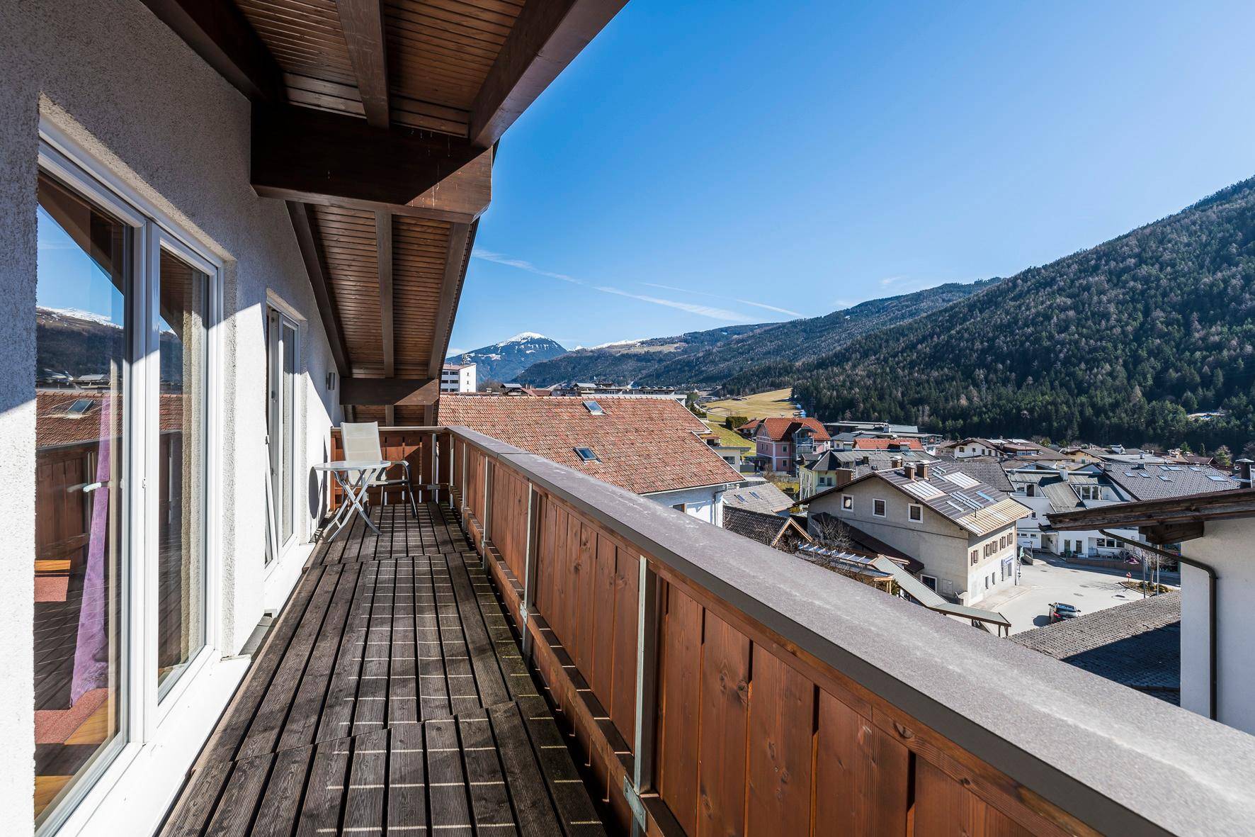 Langer Balkon mit Holzboden und Panoramablick auf die Berge und das umliegende Tal.
