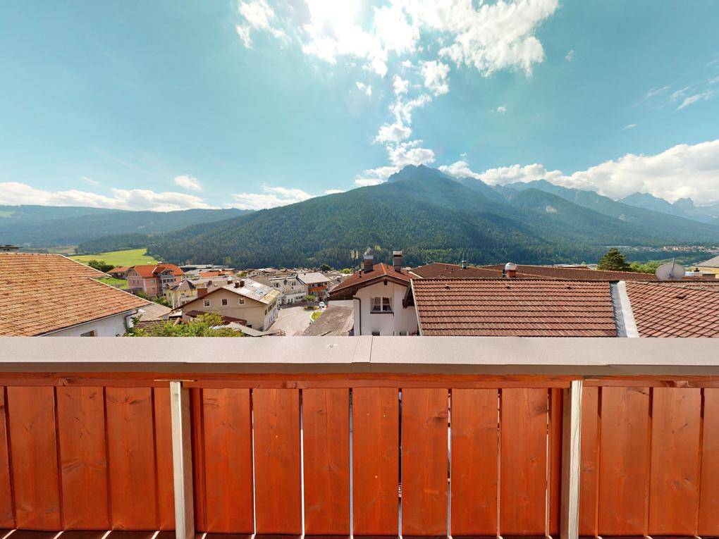 Weitläufiger Bergblick von einem Balkon mit Holzelementen unter einem blauen Himmel.