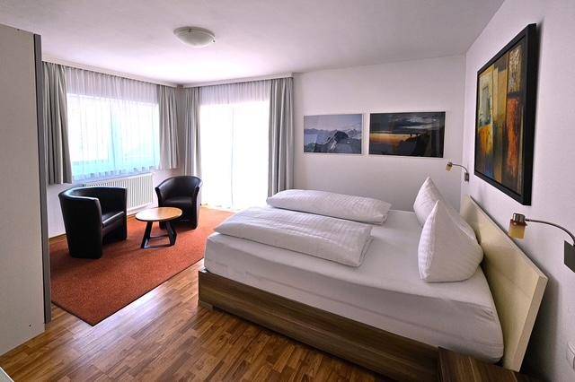 Gemütliches Schlafzimmer mit Doppelbett, Sitzgelegenheit und Holzboden unter großen Fenstern.