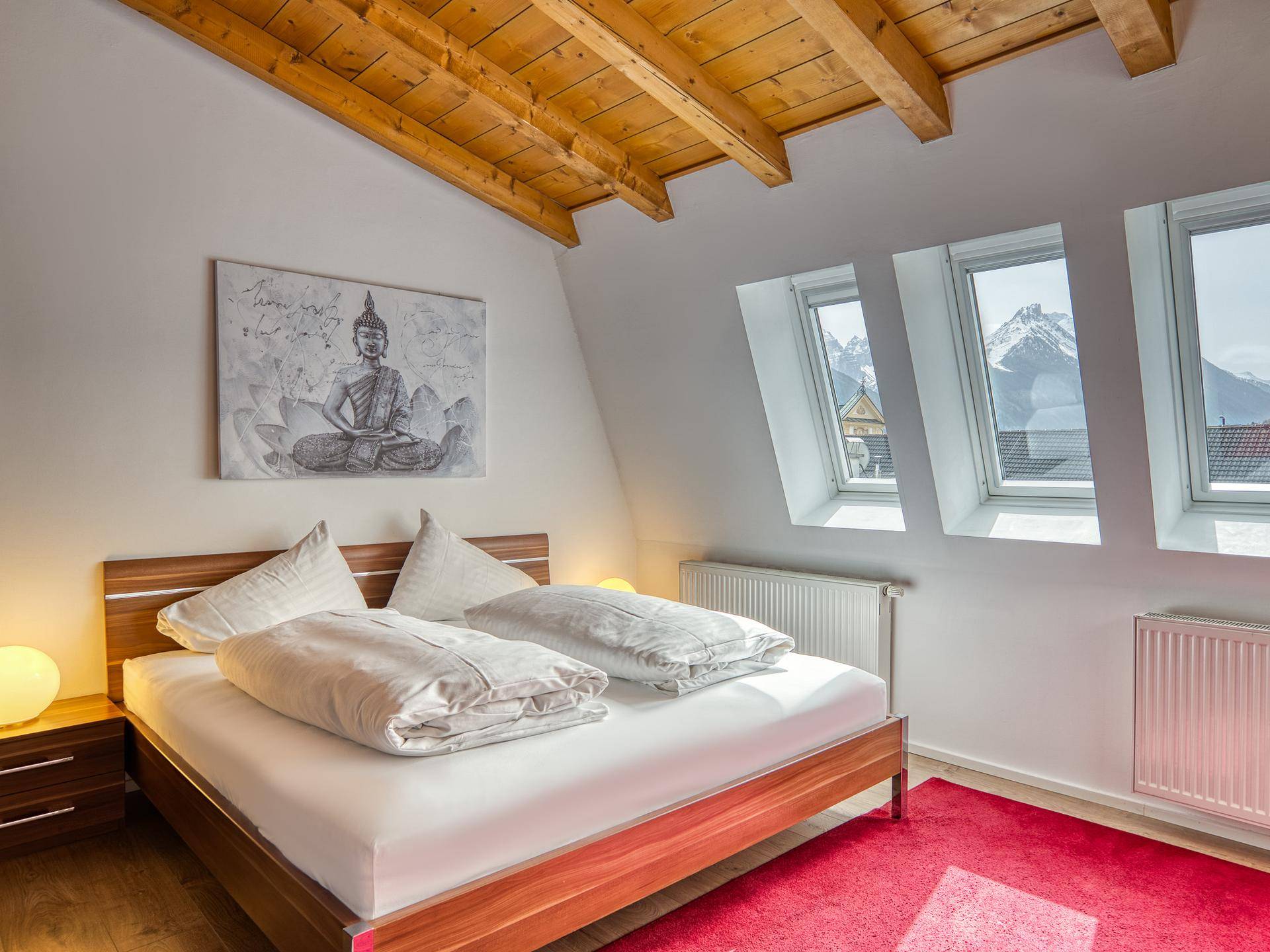 Gemütliches Schlafzimmer mit Holzbalkendecke, Doppelbett und Dachfenstern mit Bergblick.