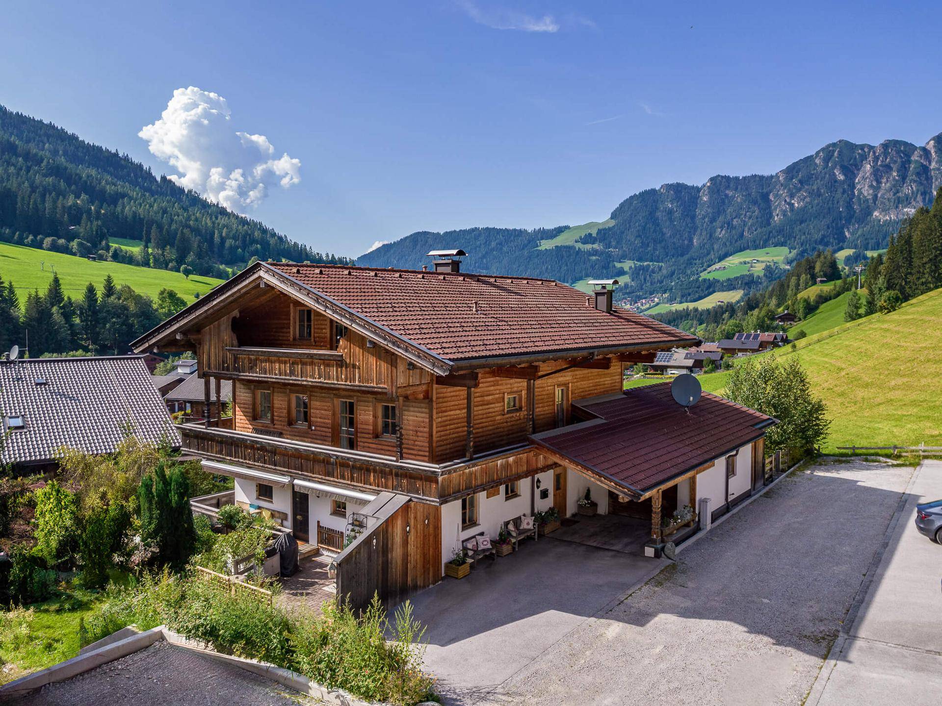 Traditionelles Holzhaus im alpinen Stil mit Satteldach, umgeben von grünen Bergen und Wiesen.