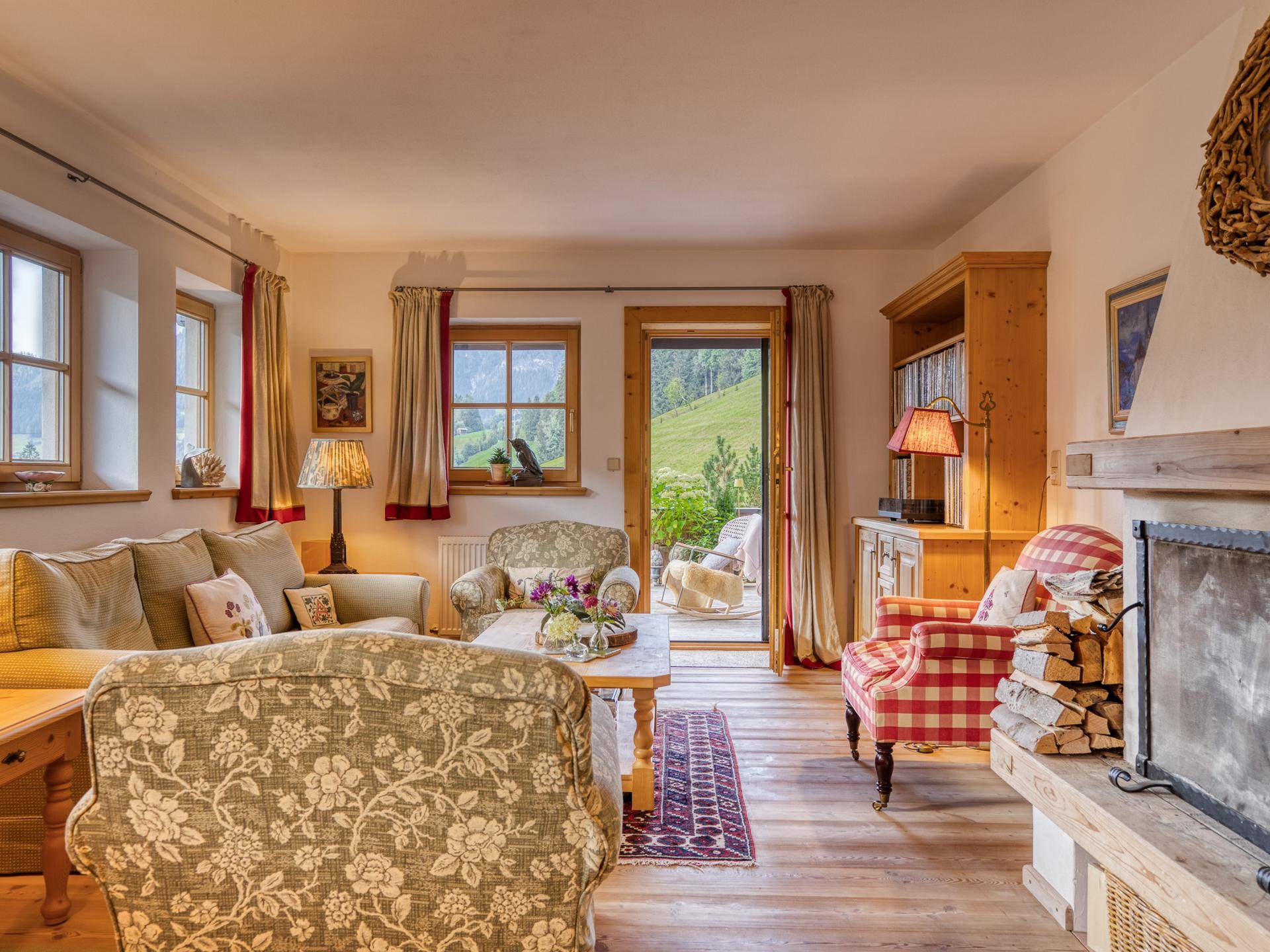 Gemütliches Wohnzimmer im alpinen Stil mit Kamin, Holzboden und Zugang zur Terrasse.