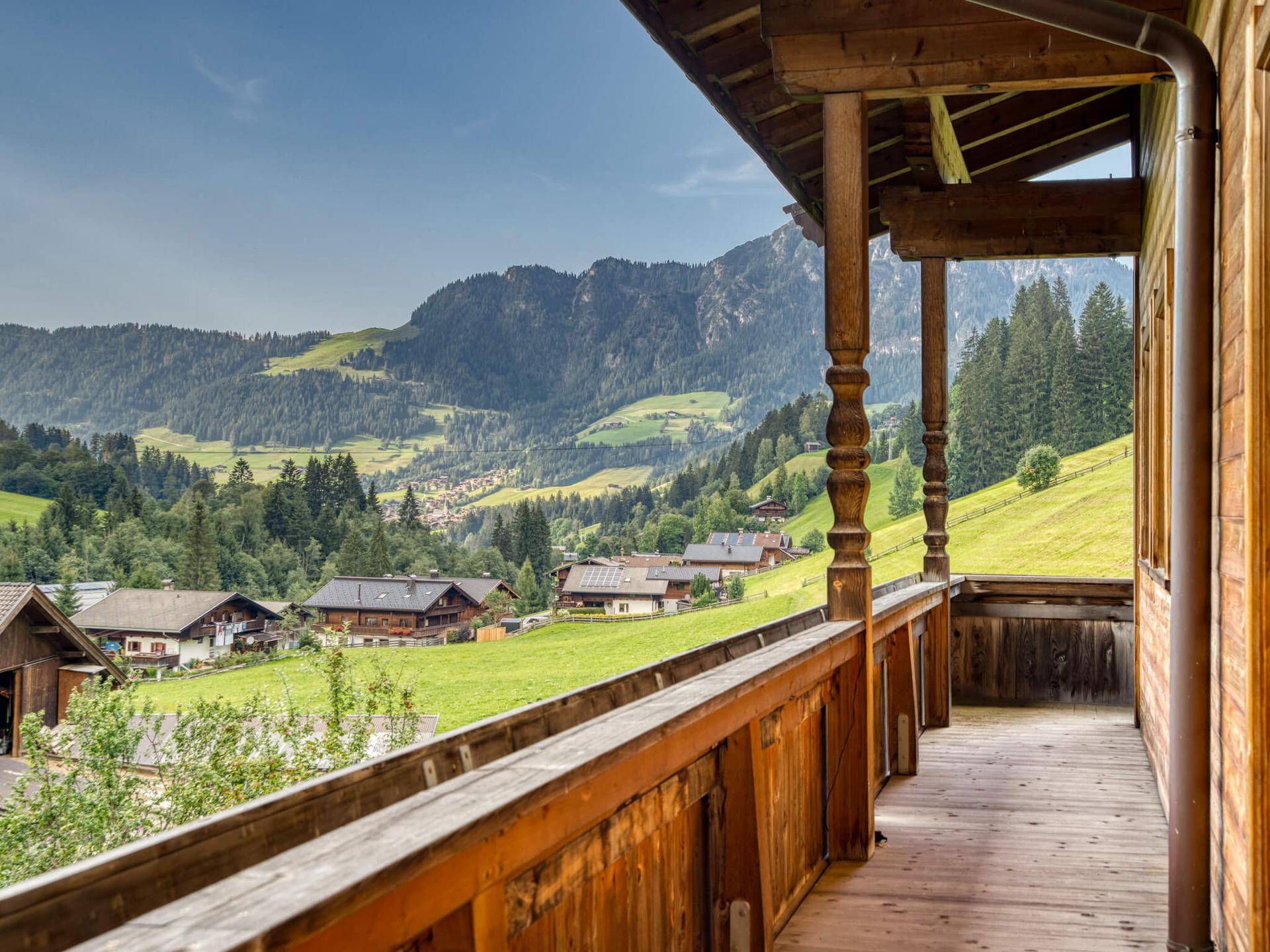 Langer Holzbalkon mit traditionellem Geländer und weitem Blick über das Tal und die Berge.
