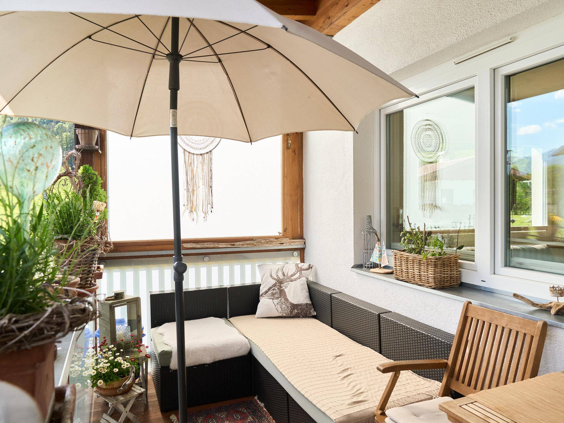 Gemütlicher Balkon mit bequemen Sitzgelegenheiten, Sonnenschirm und vielen Pflanzen.