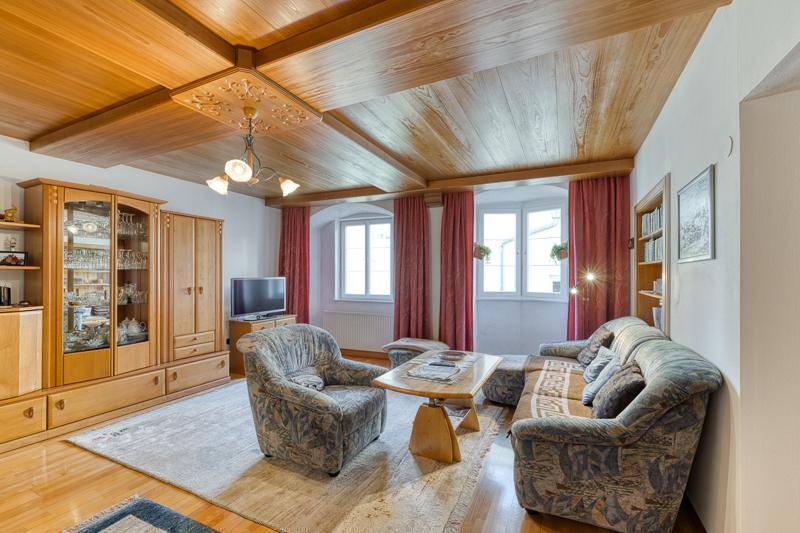 Gemütliches Wohnzimmer mit Holzbalkendecke, traditionellen Möbeln und roten Vorhängen.