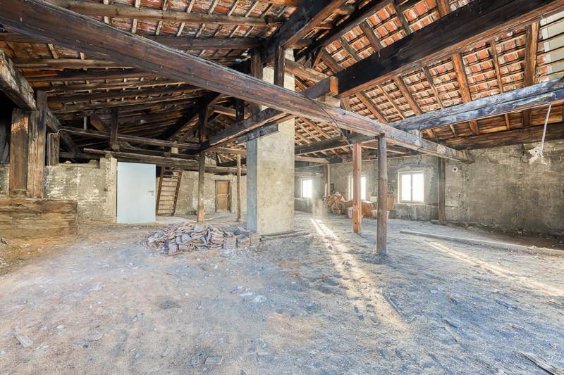 Unausgebauter Dachboden mit sichtbaren Holzbalken und Ziegeln, bereit für den Ausbau.