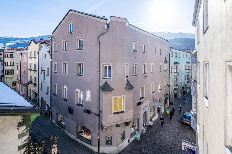 Panoramablick auf eine belebte Straßenecke mit historischen Gebäuden und schneebedeckten Bergen.